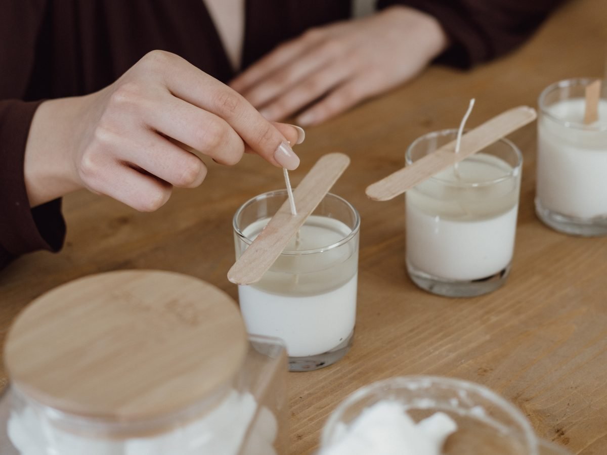 Mains disposant les mèches dans des verres de bougie remplis de cire, sur un établi en bois