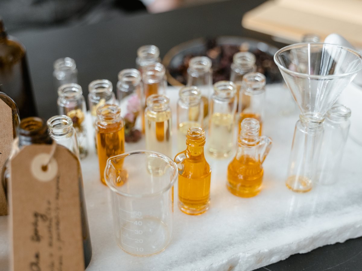 Fioles d'huiles essentielles étiquetées à la main, éprouvette graduée et entonnoir sur le plan de travail en marbre de l'atelier Myalem